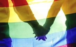 People, homosexuality, same-sex marriage, gay and love concept - close up of happy male gay couple hugging and holding rainbow flag